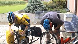 Tao makes adjustments to his brakes after already adjusting his hubs and headset outside Schaan youth hostel, while Joe just adjusts his brakes